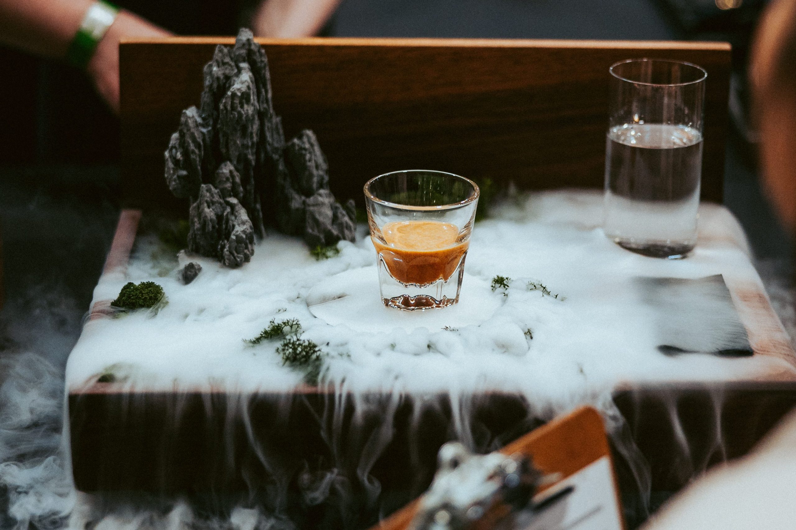 an espresso on a tray with dry ice smoke and a small sculpture of a mountain 