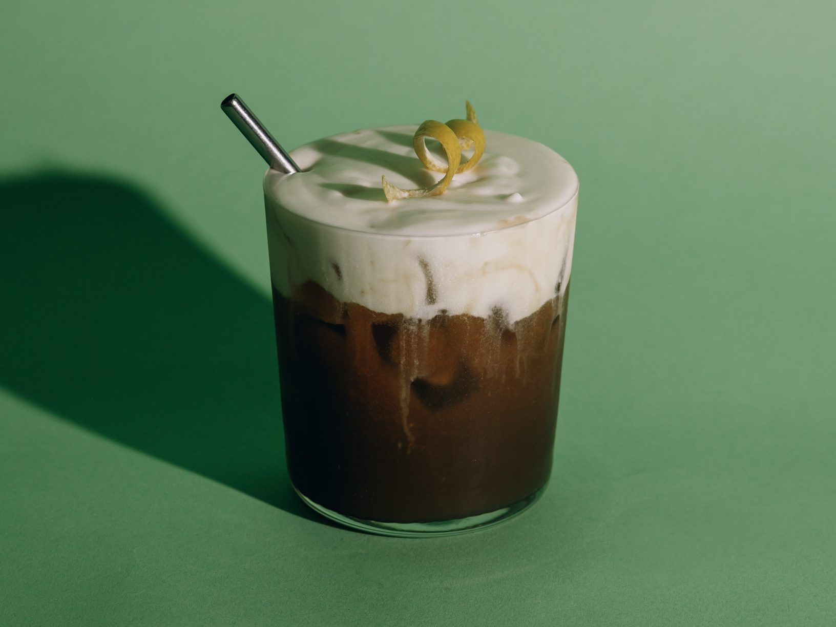 an iced coffee specialty drink with heady cold foam on top and a citrus garnish