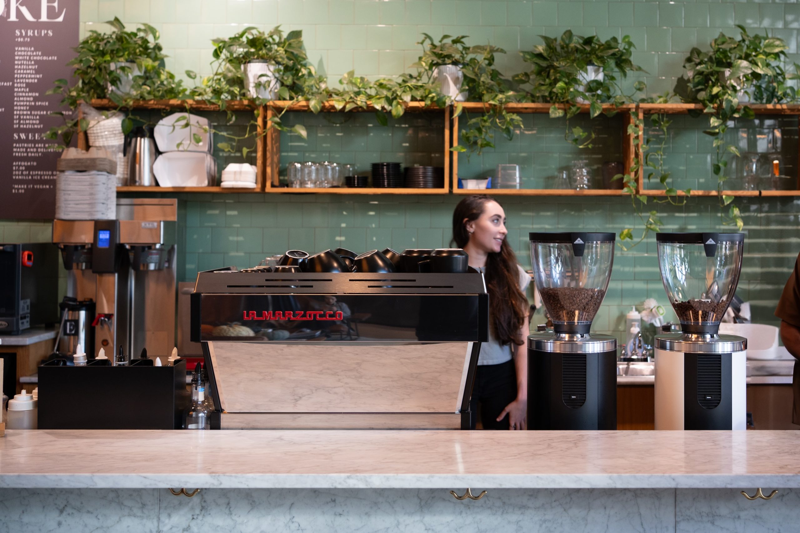 a barista behind a la marzocco espresso machine and two sync grinders