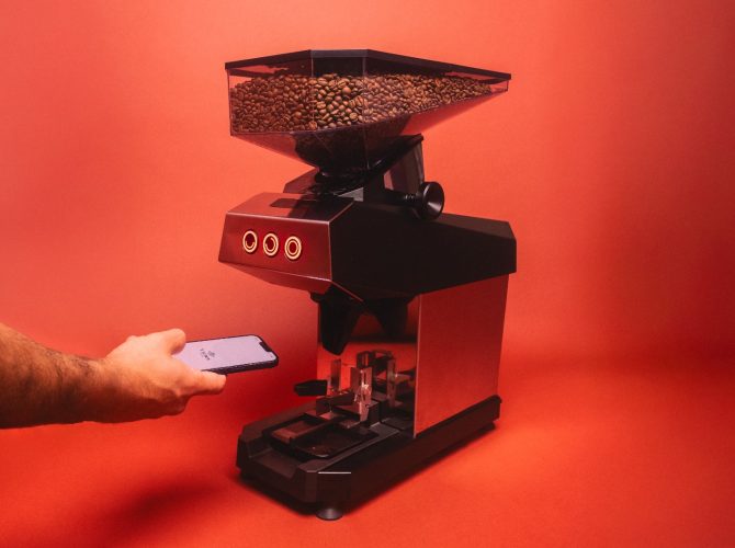 a lamarzocco swan grinder with grind-by-weight and connected scale with an arm holding a phone showing the new la marzocco app on a red background