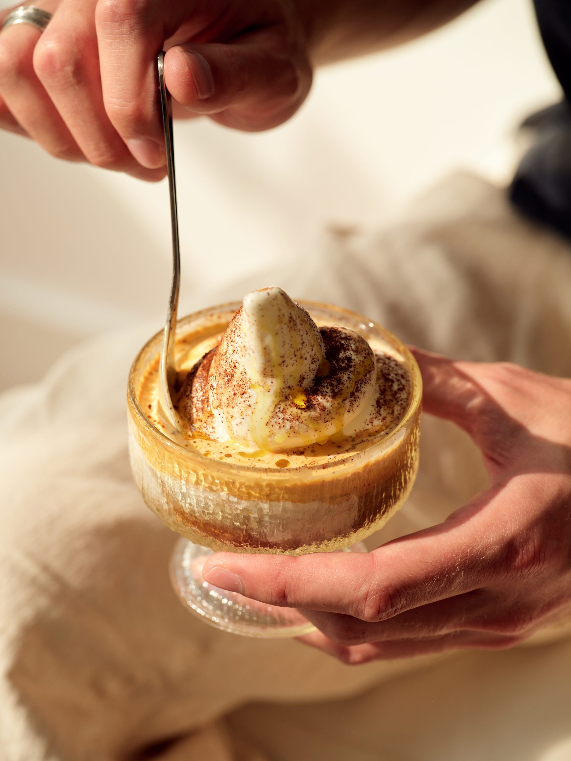 a hand stirirng an affogato with a spoon. the ice cream has coffee power dusted on it along with olive oil and sea salt