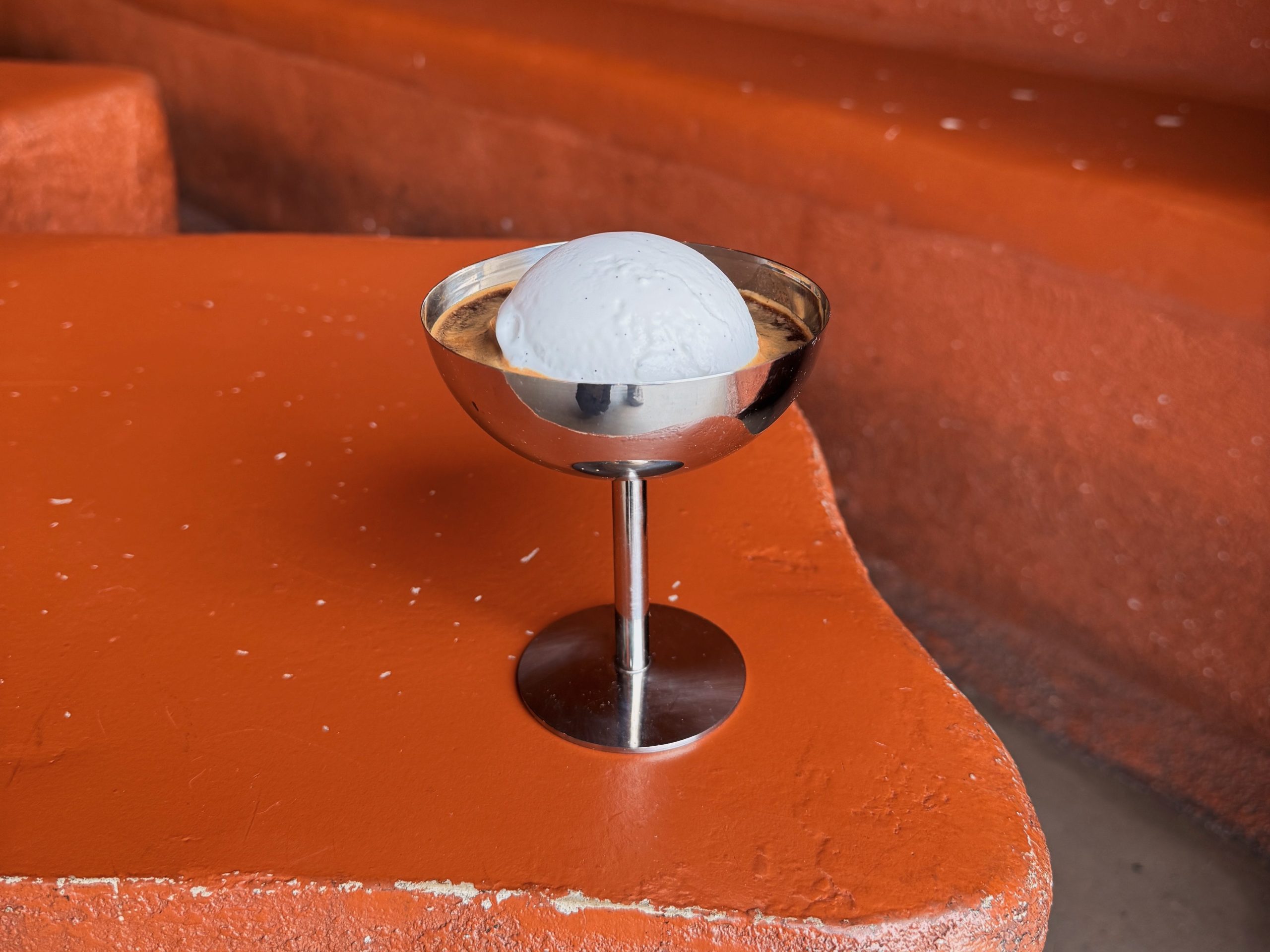 a scoop of ice crema floating on espresso in a silver goblet on a way orange background