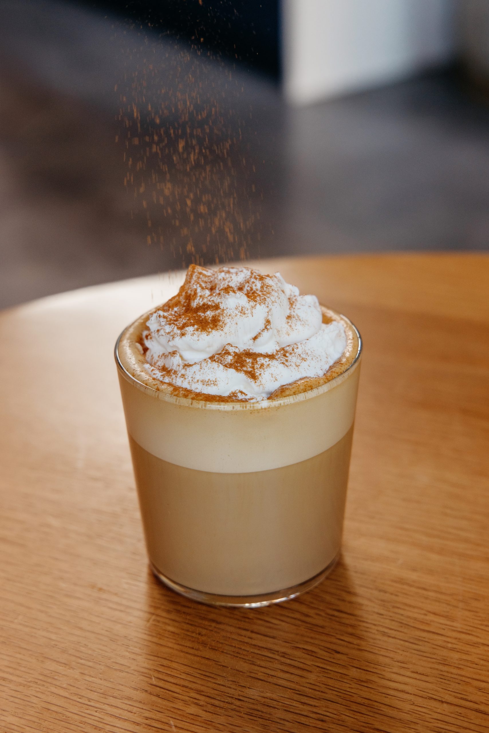 a fall drink with whipped cream on top in a glass with cinnamon being dusted on top