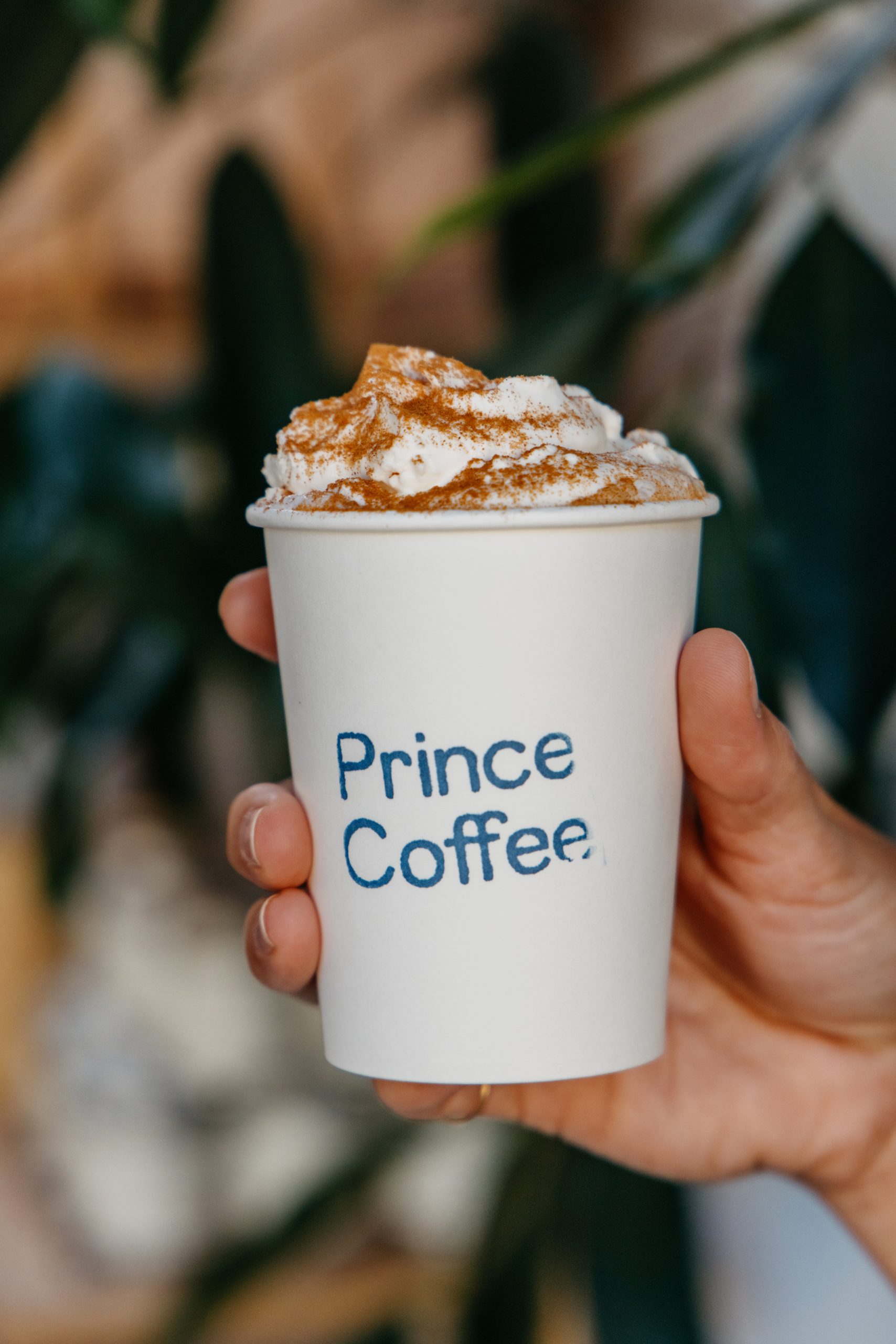 a paper cup with prince coffee stamped on it with a fall drink with whipped cream on top
